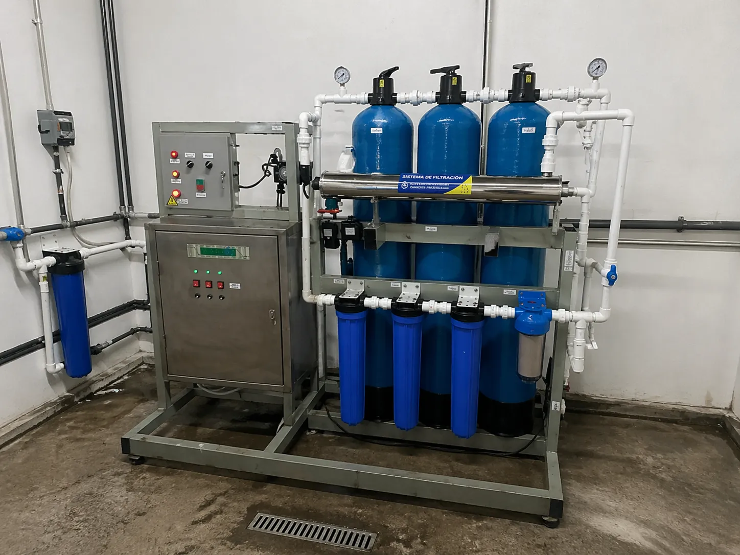 Sistema industrial de filtración de agua con tanques azules, filtros y panel de control instalado en sala técnica.